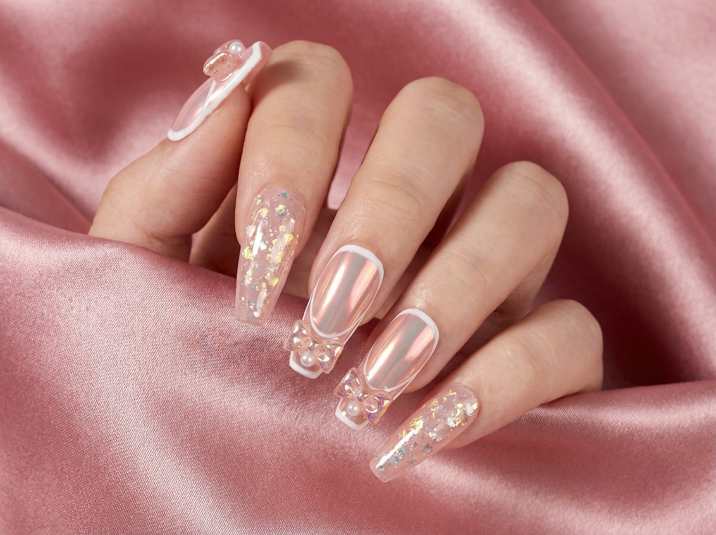Hand model wearing pink chrome coffin nails with decorative bows
