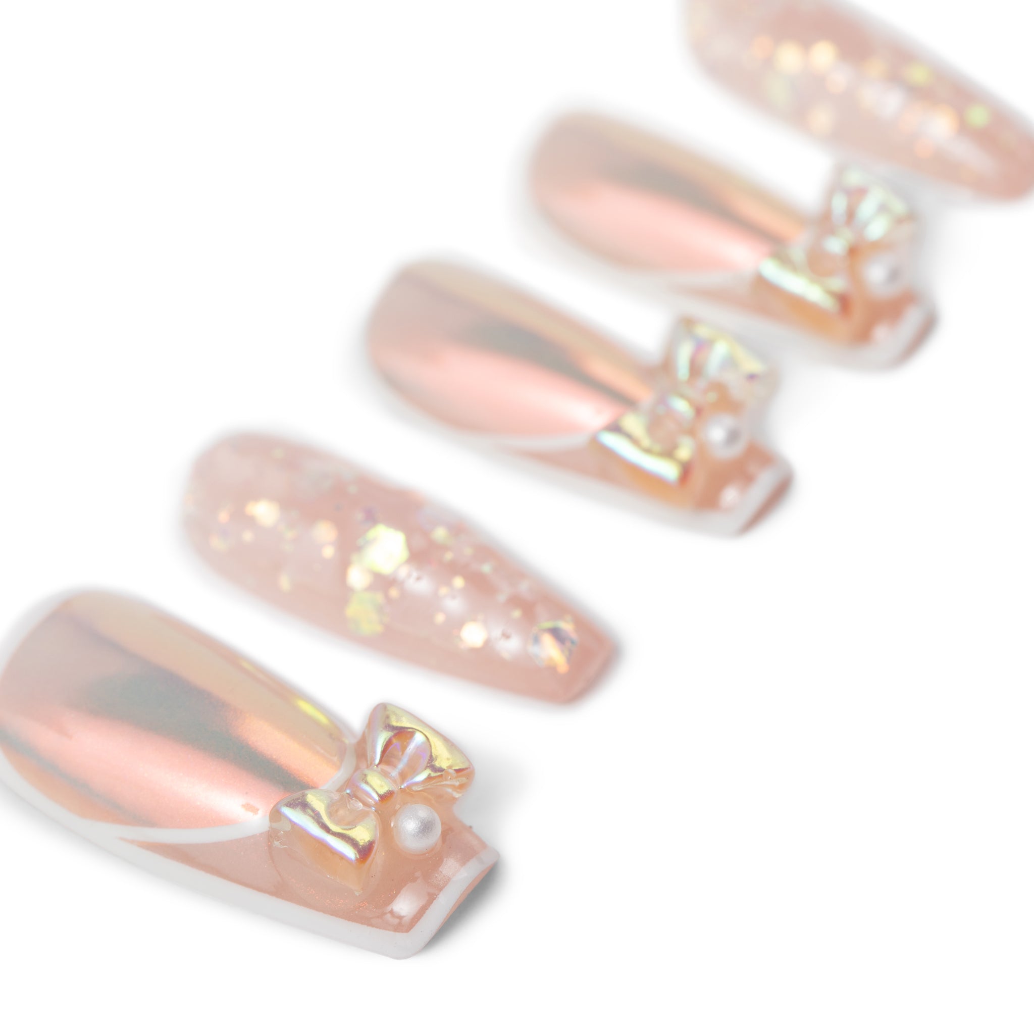 Sixaloa Cosmetics pearl bow press-on nails - scattered detail view of peach chrome coffin nails showing the gold bow and pearl charms up close on white