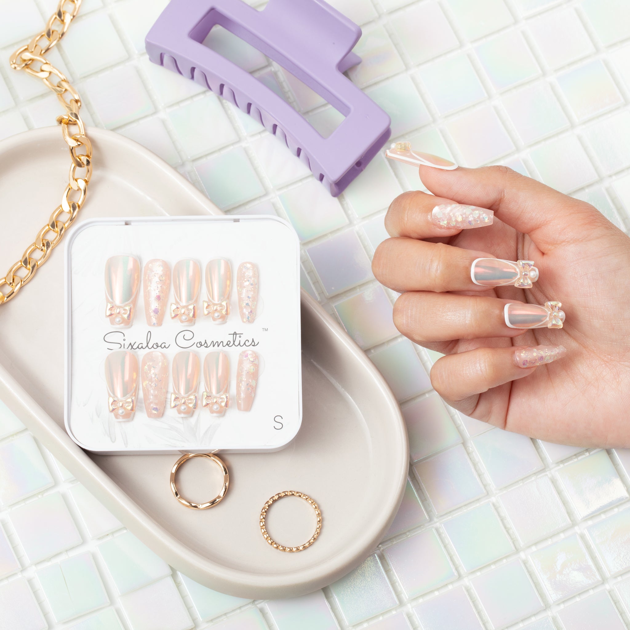 Sixaloa Cosmetics pearl bow press-on nails vanity flat lay with the size Small tin, jewelry and a claw clip styled on a soft background